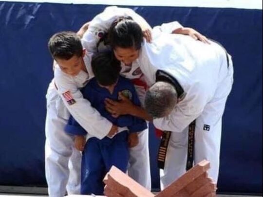 Master Duque bows while hugging his three children over a pile of broken bricks