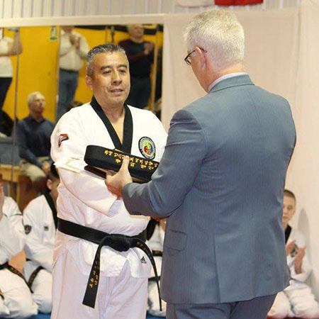 Man with white hair gives a 6th dan belt in taekwondo to martial arts master.