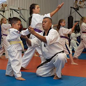 Taekwondo master on his knees instructs young student on form technique.