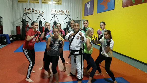 Taekwondo master and female self defense students pose in fighting stance.