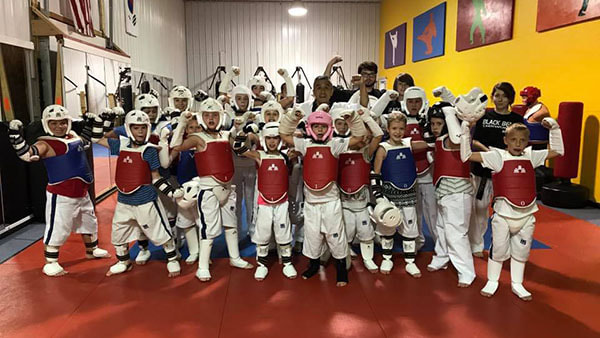 Taekwondo master and instructors stand behind color belt students in their sparring gear.