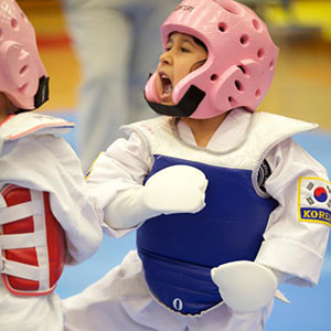 Young student in pink helmet and blue chest gear kiyups while she spars.